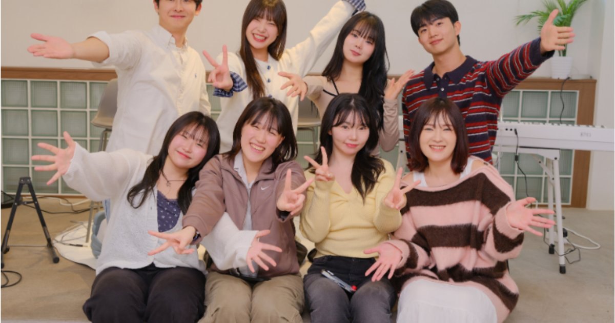 유리블록 창과 하얀 건반이 놓인 밝은 방에서 여덟 명이 바닥에 앉거나 뒤에 서서 손을 펼치고 웃는 모습