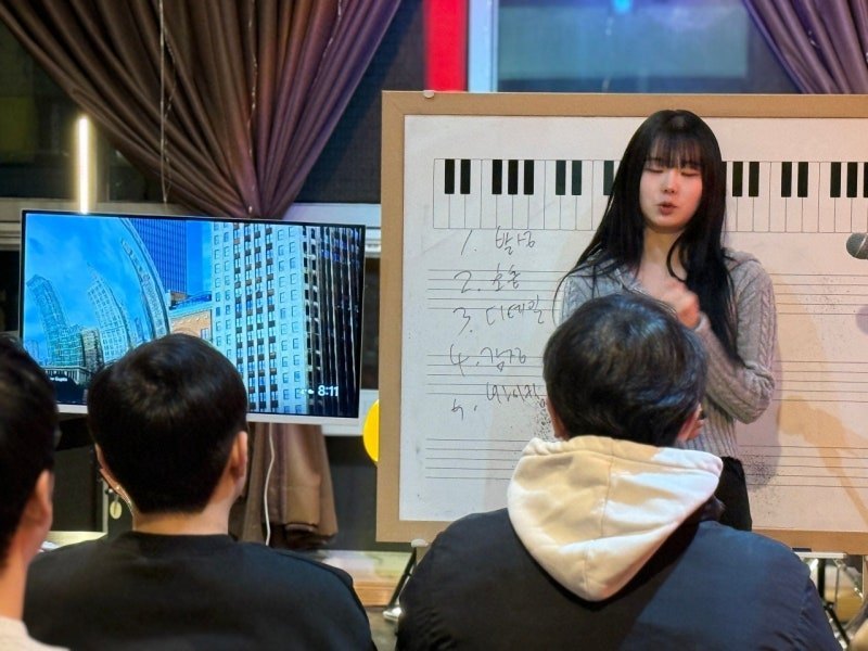 건반 그림이 그려진 화이트보드 앞에서 강사가 설명하고 수강생들이 앉아 듣는 모습